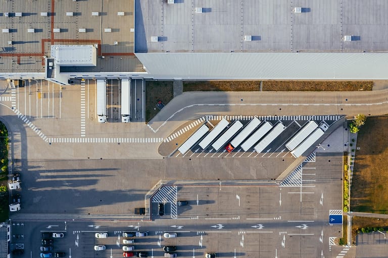 Luftaufnahme eines Logistikzentrums mit Hallendach, Laderampen, Lkw-Aufliegern und Parkplatz