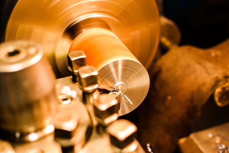 Nahaufnahme einer Drehmaschine: ein Drehmeißel bearbeitet ein rotierendes Metallwerkstück in warmem, goldenem Licht