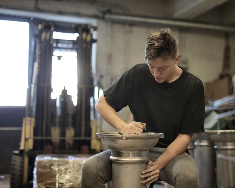 Junger Mann bearbeitet in einer Metallwerkstatt eine Stahlschale auf einem Ständer