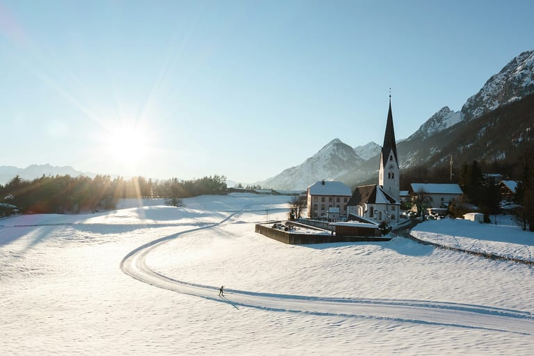 Verschneite Kirche in Gnadenwald mit Langlaufloipe in der Wintersonne