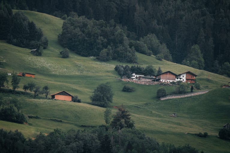Steile Bergwiesen mit Holzstadeln und einem Bauernhof bei Haiming im Tiroler Oberland