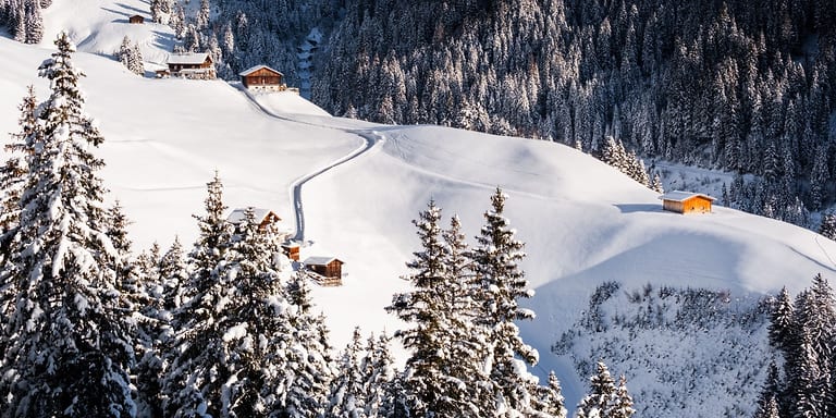 Verschneite Almhütten und ein Winterweg zwischen tief verschneiten Fichten im Zillertal